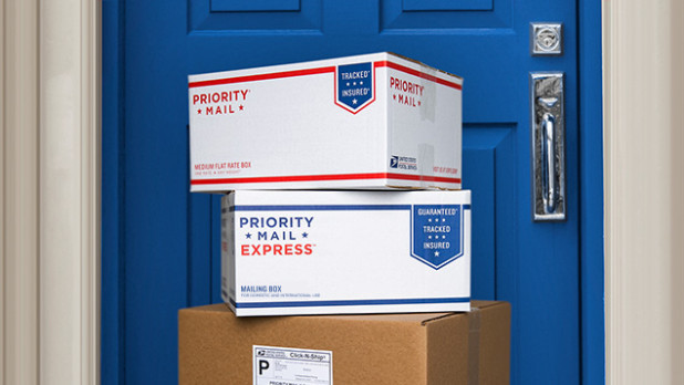 Stack of USPS Priority Mail shipping boxes in front of a door.