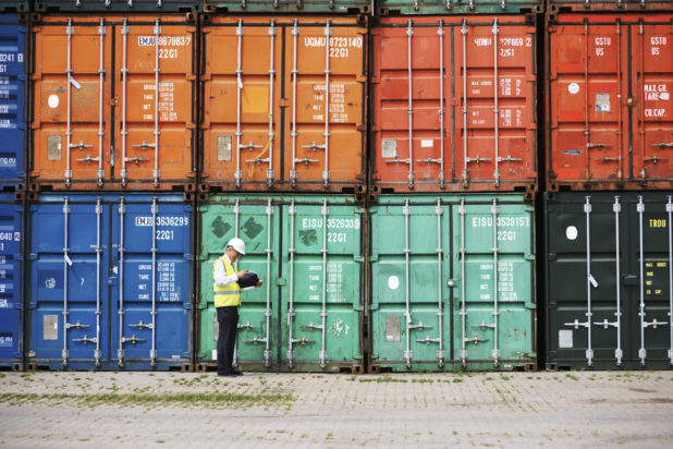 A foreman standing in front of a stack of colorful containers and making notes.