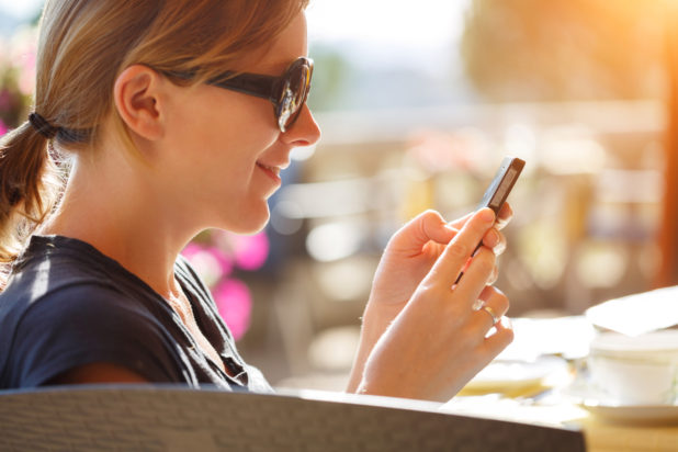 Portrait of happy woman reading off touch phone in cafe outdoors.