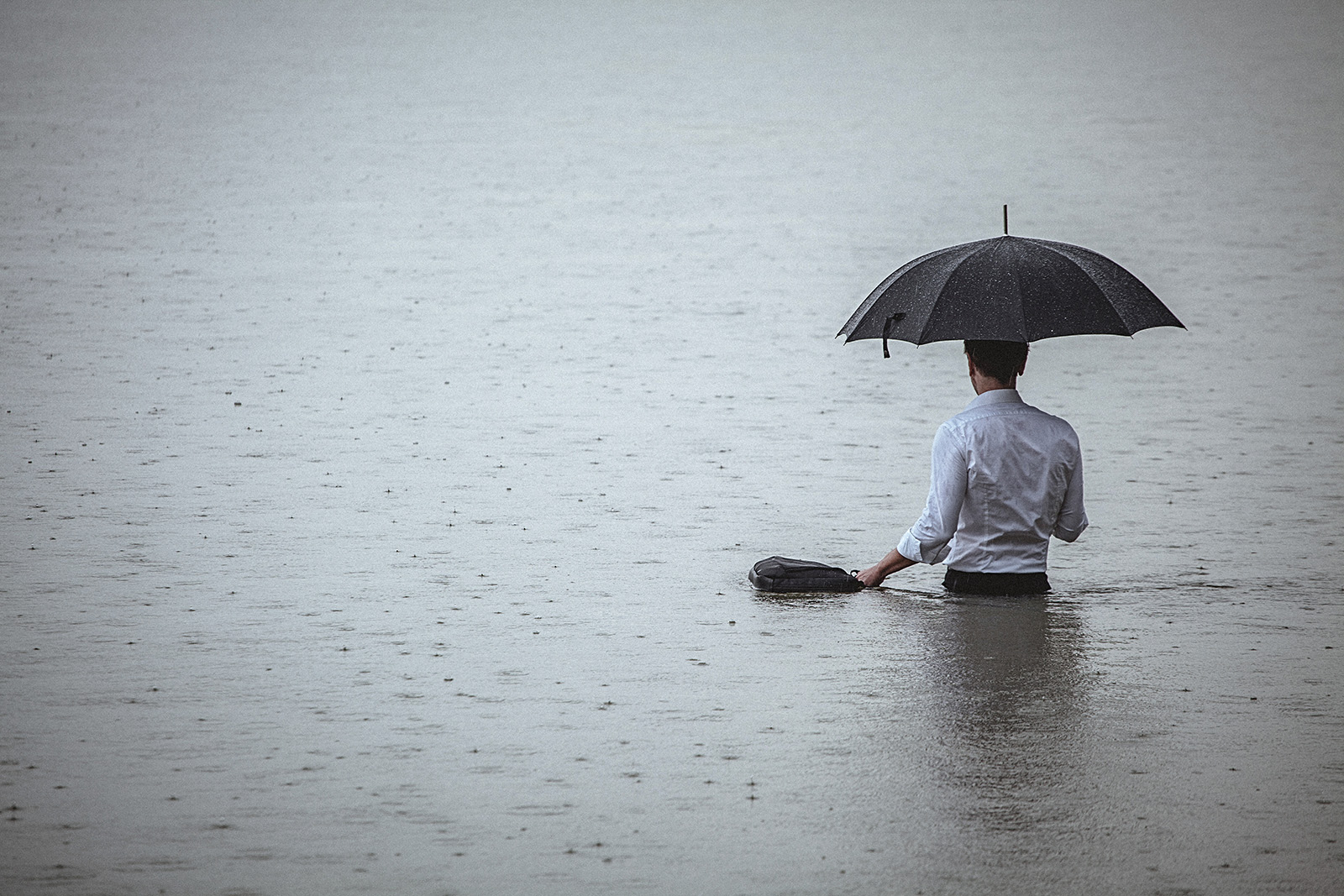 Man standing in water and holding umbrella and briefcase during rain